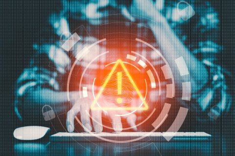 Graphic of a person sitting at a keyboard with a hologram of an alert signal superimposed. Photo credit: Adobe Stock