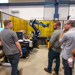 Photo of five men looking at a robotic arm at the ARM Institute