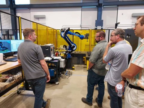 Photo of five men looking at a robotic arm at the ARM Institute