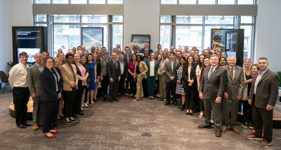 A group of people in business attire stand in front of windows. 