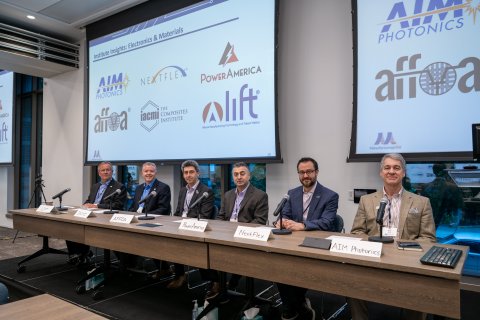 Six men sit at a long table. On the wall behind them are screens displaying institute logos.