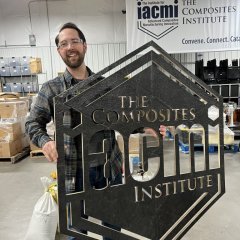 Photo of Vitriform3D CEO, Alex Stiles, holding up a composite sign of the IACMI logo