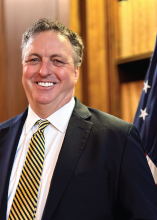Photo of Mark Schmit standing in front of an American flag