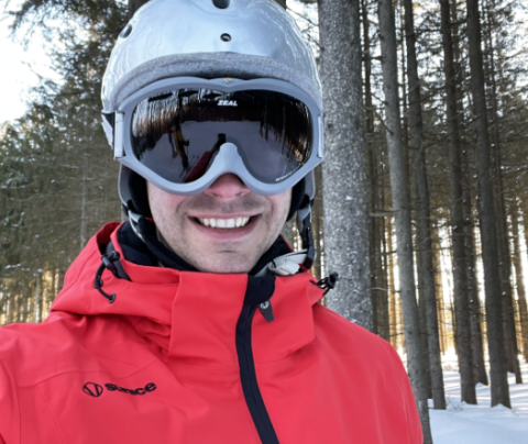 Photo of Glenn Cormack skiing in a red jacket wearing a silver helmet and goggles.